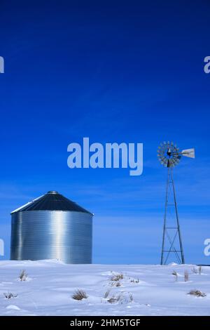 Windmühle und Stahlkornsilos im Winterschnee mit blauem Himmel auf dem Bauernhof für die landwirtschaftliche Landwirtschaft Stockfoto