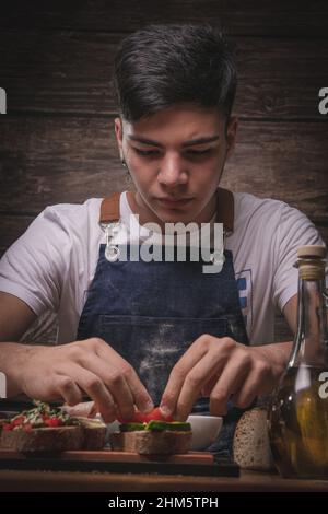 Schöner junger Mann Koch kocht Brot auf einem Holztisch und Holzhintergrund Stockfoto