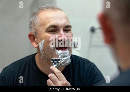 Ein hübscher Mann mittleren Alters, der sich im Badezimmer den Bart rasiert Stockfoto