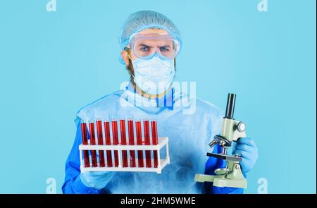 Arzt in medizinischer Maske mit Reagenzgläsern und Mikroskop. Wissenschaftler analysiert Blutprobe in der Klinik. Stockfoto