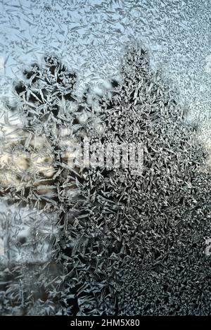 Eiskalte Frost-Kristalle Muster auf Glasfenster des Hauses in der Landschaft, mit Kiefern immergrünen Bäumen draußen während des Sonnenuntergangs, Browntown, Wisconsin, USA. Stockfoto
