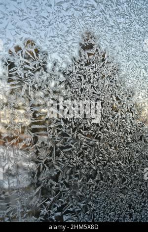 Eiskalte Frost-Kristalle Muster auf Glasfenster des Hauses in der Landschaft, mit Kiefern immergrünen Bäumen draußen während des Sonnenuntergangs, Browntown, Wisconsin, USA. Stockfoto