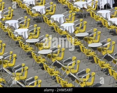 Schräge Reihen mit gelben Stühlen und weißen Tischen am Morgen auf dem Markusplatz in Venedig, von oben betrachtet. Stockfoto