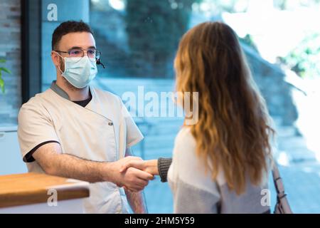 Der Patient begrüßt die Empfangsdame des Gesundheitszentrums mit einem Händedruck Stockfoto