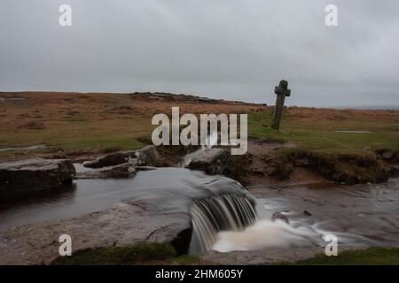 Windy Post, ein geneigtes Granitkreuz, das auf einem Moorland an einem Fluss im Dartmoor-Nationalpark in Devon steht Stockfoto