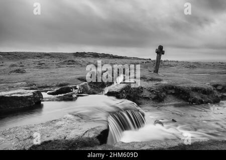 Windy Post, ein geneigtes Granitkreuz, das auf einem Moorland an einem Fluss im Dartmoor-Nationalpark in Devon steht Stockfoto