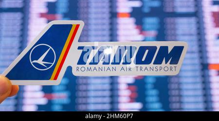 11. Dezember 2021, Bukarest, Rumänien. Das Emblem der Fluggesellschaft TAROM vor dem Hintergrund einer elektronischen Tafel mit einem Flugplan auf der int Stockfoto