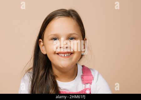 Porträt eines Kindes mit leuchtend leuchtenden Augen und aufgeregt glückliches Lächeln mit oberen Zähnen Blick auf die Kamera in leuchtend rosa Jumpsuit und weißem T-Shirt Stockfoto