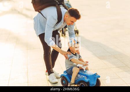 Papa lehrt seinen kleinen Sohn, ein Kinderauto im Park zu fahren, Balance zu halten, Spaß mit der Familie zu haben. Vater und Sohn im Park, der Junge ist drivin Stockfoto