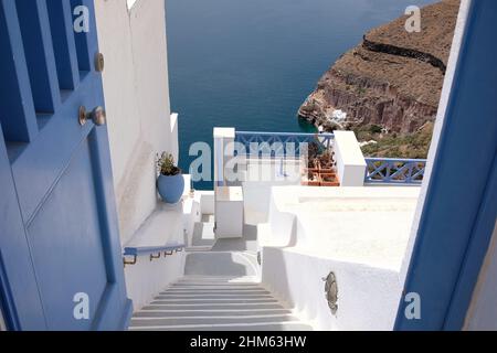 Santorini, Griechenland - 7. Mai 2021 : Eine Tür und eine Treppe führen zu einem Wohngebäude mit einem schönen Blick auf die Ägäis und den Vulkan Santor Stockfoto