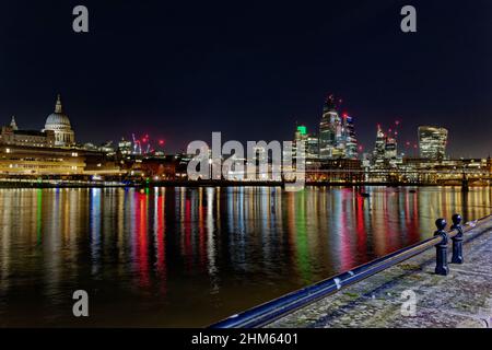 Farbenfrohe Reflexionen in der Themse von den Lichtern des Londoner Finanzzentrums mit seinen verschiedenen Wolkenkratzern, die die Nacht erleuchten Stockfoto