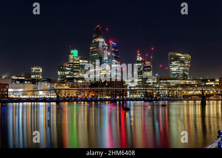 Farbenfrohe Reflexionen in der Themse von den Lichtern des Londoner Finanzzentrums mit seinen verschiedenen Wolkenkratzern, die die Nacht erleuchten Stockfoto