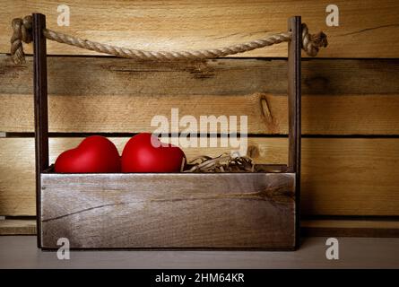 Zwei große rote Herzen im Korb auf einem hölzernen Hintergrund Stockfoto