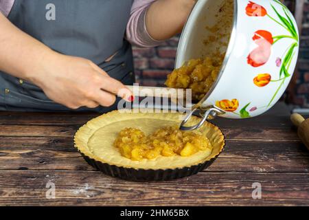 Frauen bereiten köstliche Apfeltorte oder Kuchen groß auf Holztisch Hintergrund.Spredding die gekochten kandierten Apfel über den Teig Stockfoto