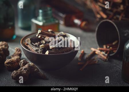 Schwarze Schale mit gemeinsamen Beinwell- oder symphytum officinale-Wurzeln. Getrocknete comfrey officinalis Wurzeln, Knitbone und Bistort, Schlangenfutter. Flaschen mit Infusion und Stockfoto