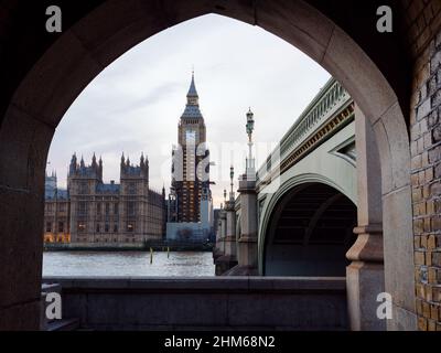Houses of Parliament und Westminster Bridge von einem Torbogen am Südufer der Themse aus gesehen. Stockfoto