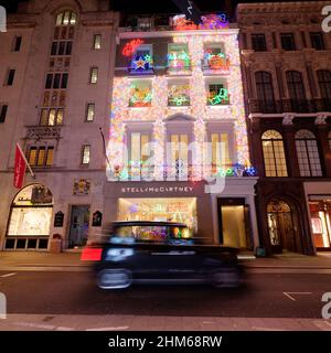 Stella McCartney Fashion Store in der Old Bond Street, während sich das Weihnachtslicht in einem vorbeifahrenden Taxi widerspiegelt. London. Stockfoto