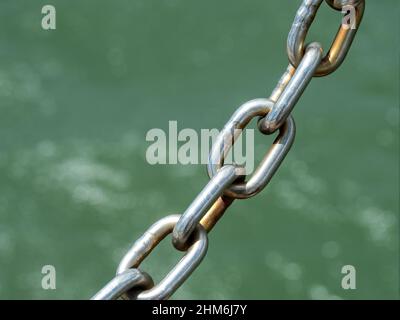 Sicherheit geht vor. Dicke, silbergraue Kettenglieder aus Metall. Verbunden vor blaugrünem Meerwasser im Hafen. Sicherheit! Verbunden Stockfoto