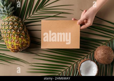 Weibliche Hand mit unbeschriftete Karte, Früchte und Palmblätter auf farbigem Hintergrund Stockfoto
