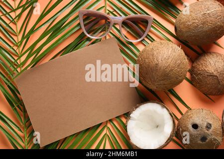 Komposition mit leerer Karte, Kokosnüssen, Palmblättern und Sonnenbrille auf farbigem Hintergrund Stockfoto