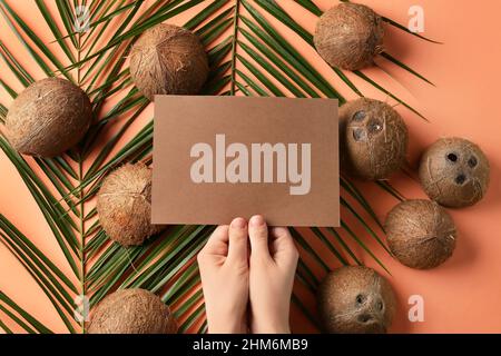 Weibliche Hände mit leerer Karte, Kokosnüssen und Palmenblättern auf farbigem Hintergrund Stockfoto