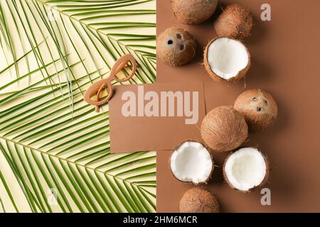 Komposition mit leerer Karte, Sonnenbrille, Kokosnüssen und Palmblättern auf farbigem Hintergrund Stockfoto