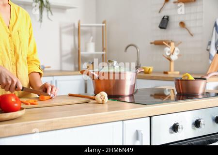 Kochgeschirr und eine Frau schneiden Karotten auf Holzbrett in der Küche Stockfoto