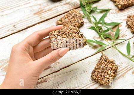 Frau mit Proteinriegel mit Hanfsamen und Blättern auf weißem Holzhintergrund Stockfoto