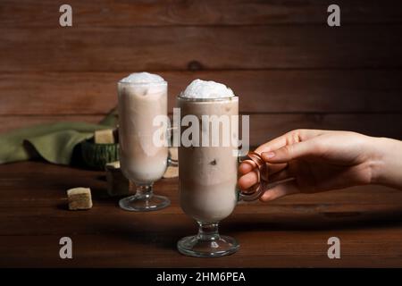 Frau mit einem Glas vereisten Hojicha Latte auf einem Holztisch Stockfoto