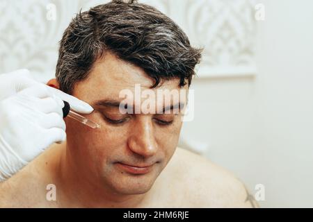 Der Kosmetologe führt Anti-Aging-Verfahren durch, trägt Serum mit Hyaluronsäure auf die Gesichtshaut auf Stockfoto