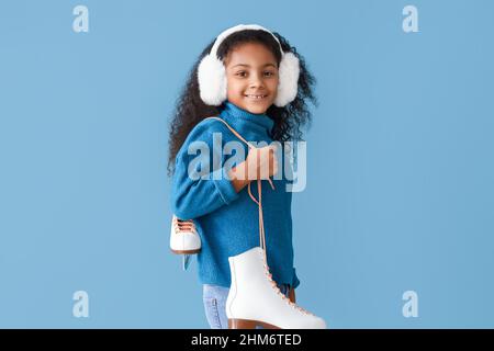 Kleines afroamerikanisches Mädchen in Ohrenschützern mit Schlittschuhe auf blauem Hintergrund Stockfoto