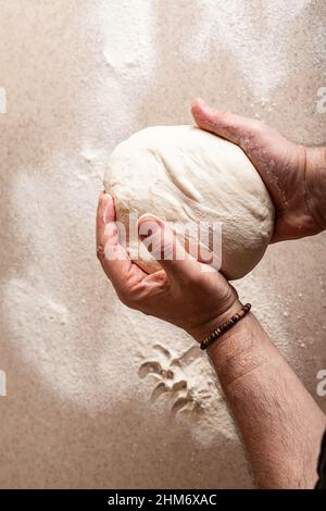 Männliche Hände kneten den Teig. Menschliche Hände bereiten Teig für hausgemachtes Baguette vor. Draufsicht. Vertikale Aufnahme Stockfoto