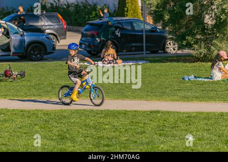 Ein Junge mit einem grünen Fahrradhelm auf dem Kopf fährt im Sommerpark mit seinem Fahrrad. Sommerpause. Junge lernen, sein Fahrrad zu fahren-April 18,2021-Richmond Stockfoto