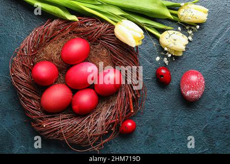 Nest mit rot bemalten Ostereiern und Blumen auf dunklem Hintergrund Stockfoto