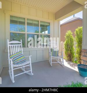 Quadratische zwei weiße Schaukelstühle mit gestreiften Kissen auf einer Veranda eines Hauses Stockfoto