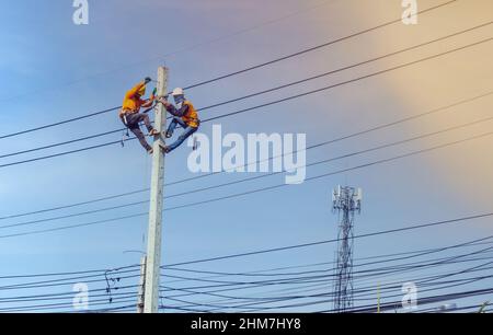 Elektriker-Linienarbeiter-Arbeiter bei Kletterarbeiten am elektrischen Pfosten-Strommast. Stockfoto