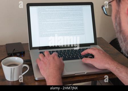 Mann, der zu Hause auf einem Laptop arbeitet und einen Text auf die Tastatur eingibt Stockfoto