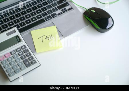 Das Wort Steuer auf gelbem Klebepapier auf dem Laptop und neben dem Rechner. Konzept der Steueranmeldung. Stockfoto