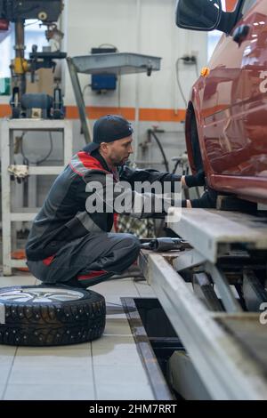 Seitenansicht Porträt eines männlichen Mechanikers, der während der Arbeit in der Autowerkstatt die Reifen am Auto wechselt Stockfoto