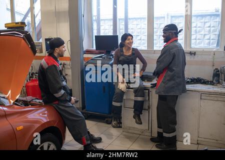 Volle Länge Blick auf verschiedene Gruppe von Mechanikern Chat während der Pause in der Kfz-Werkstatt Stockfoto