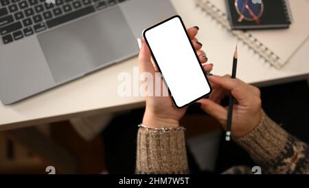 Abgeschnittene Aufnahme, Draufsicht einer Frau in kuscheligen Pullovern mit einem Modell aus weißem Smartphone-Bildschirm über dem Arbeitsplatz. Stockfoto