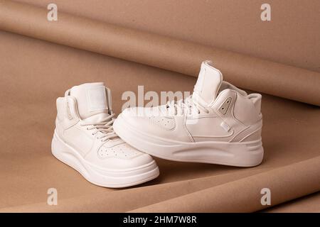 Schuhe aus Kunstleder. Ein Paar beige Sneakers auf braunem Hintergrund. Minimalistischer Style. Casual Sport Lifestyle-Konzept. Stockfoto