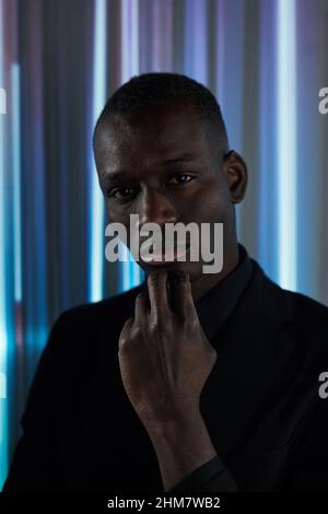 Porträt eines selbstbewussten afrikanischen Mannes in dunklem Anzug, der die Kamera im dunklen Raum betrachtet Stockfoto