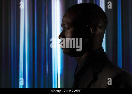 Seitenansicht eines afrikanisch selbstbewussten Mannes in elegantem dunklen Anzug, der vor dem blauen Hintergrund absieht Stockfoto
