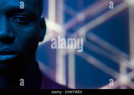 Nahaufnahme eines afrikanischen Mannes mit ernstem Ausdruck, der in einem dunklen Studio mit blauem Licht auf die Kamera blickt Stockfoto
