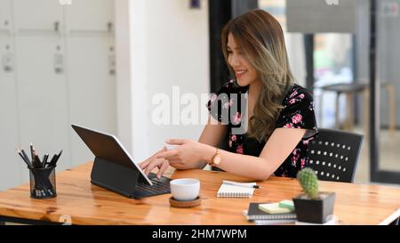 Attraktive asiatische Geschäftsfrau, die an einem digitalen tragbaren Tablet-Computer im modernen Büroarbeitsplatz arbeitet. Stockfoto
