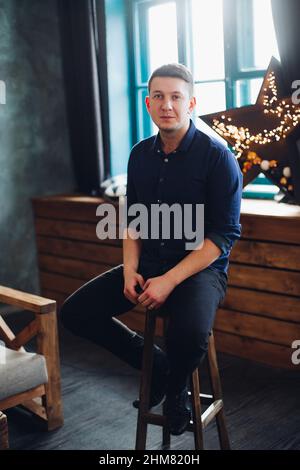 Hübscher Mann, der auf einem Stuhl in einem dekorierten Studio sitzt. Stockfoto