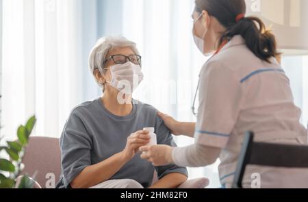 Arzt und ältere Frau mit Gesichtsmasken während des Coronavirus- und Grippeausbruchs. Virenschutz. COVID-2019. Masken übernehmen. Stockfoto