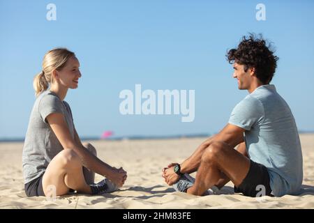 Lächelndes Paar macht Yoga-Übungen auf Sand im Freien sitzen Stockfoto