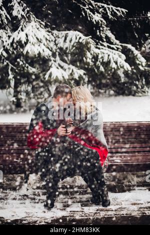 Verliebtes Paar sitzt auf der Bank und lächelnd in Schnee Wald. Stockfoto